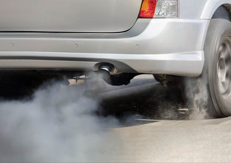 Carro soltando fumaça escura pelo escapamento que pode ser fruto de uma vela de ignição em mau estado.