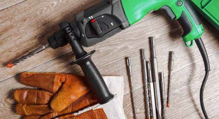 Furadeira de impacto sobre um balcão de trabalho, ao lado de luvas de proteção e brocas.