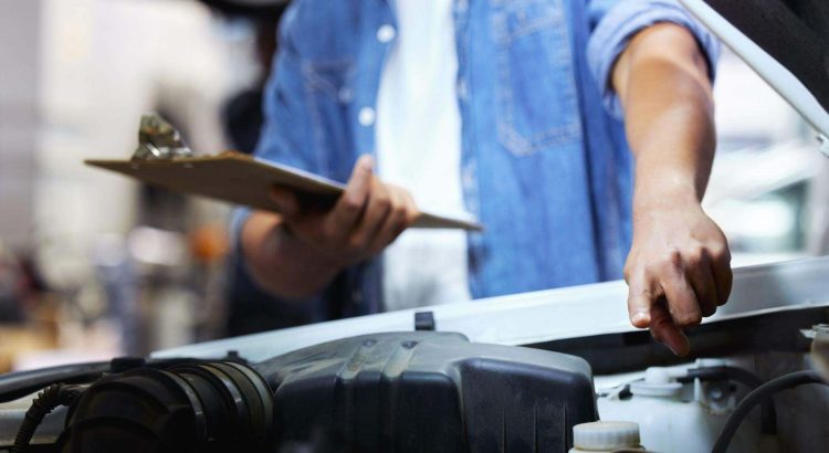 Um mecânico ou proprietário está em pé na frente de um carro com o capô aberto.